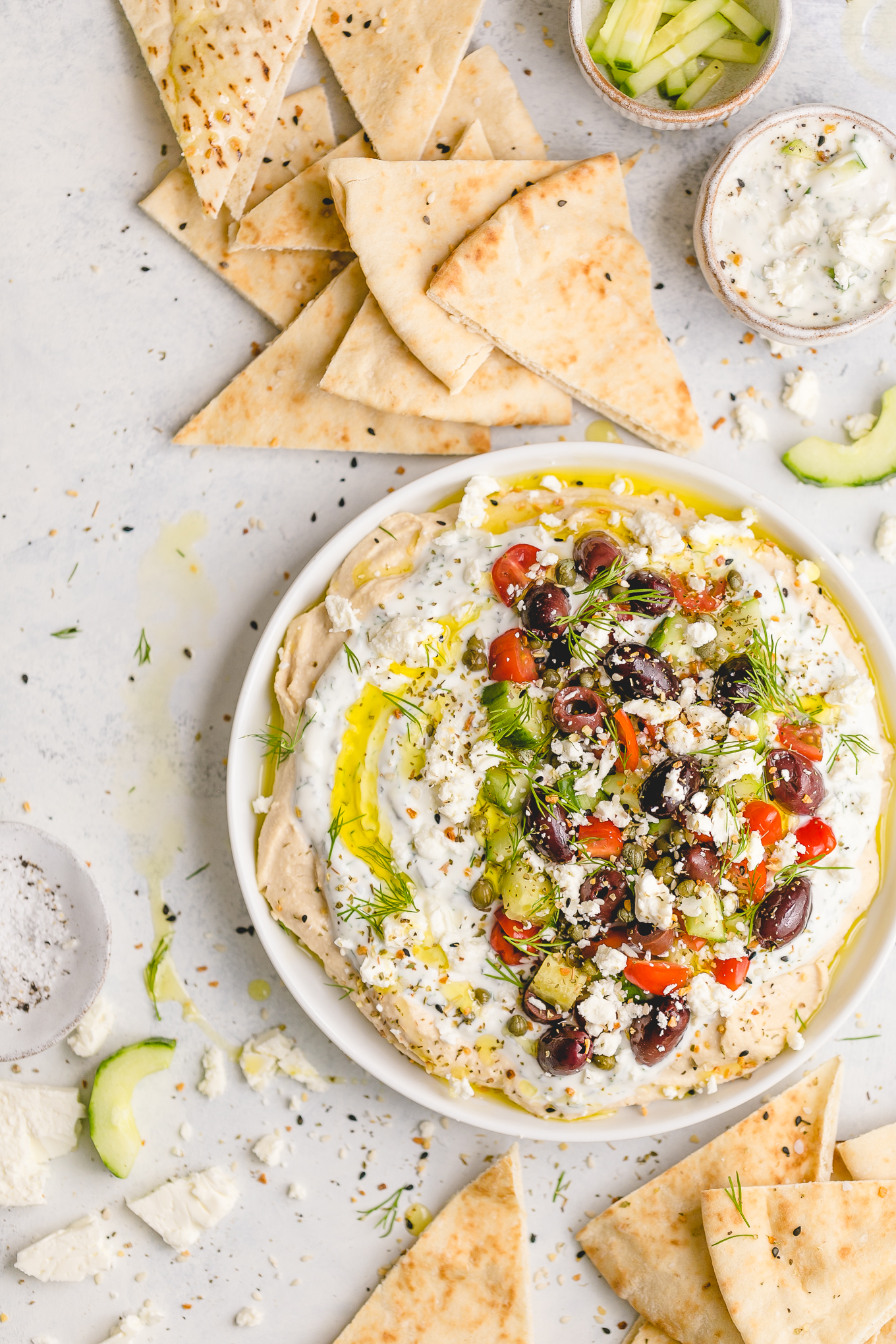 Greek Dip with Hummus and Tzatziki (134 calories) - a flavor-packed appetizer you can make a head of time! One layer of smooth, savory hummus, a layer of cool, herby tzatziki, and toppings like feta cheese, chopped fresh cucumbers, sweet tomatoes, and briney capers and olives.