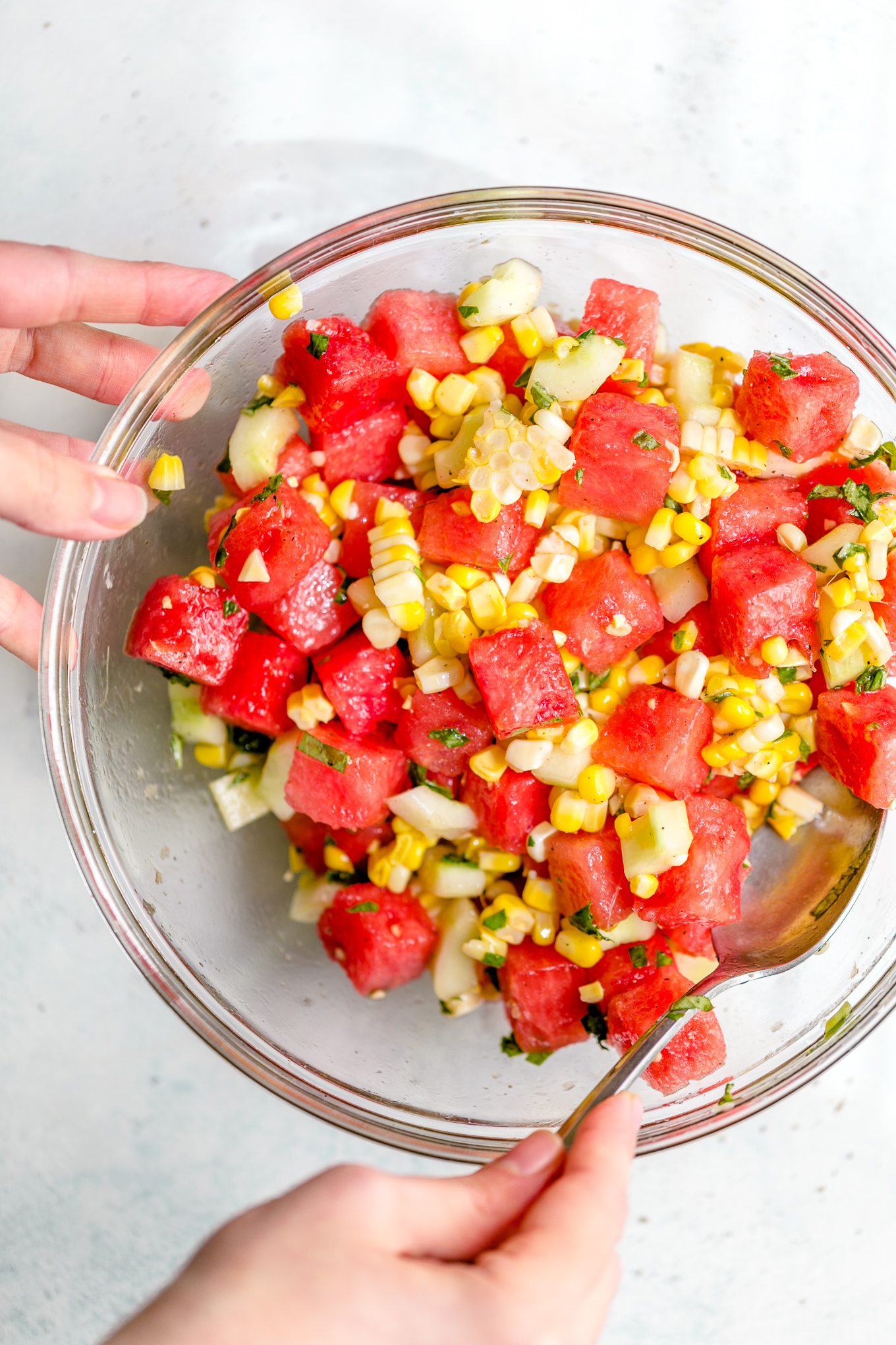 Mixing watermelon feta salad in a glass bowl